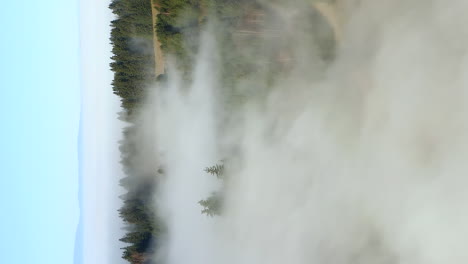 Vertical-format-flyover-above-mountain-peak-on-foggy-morning