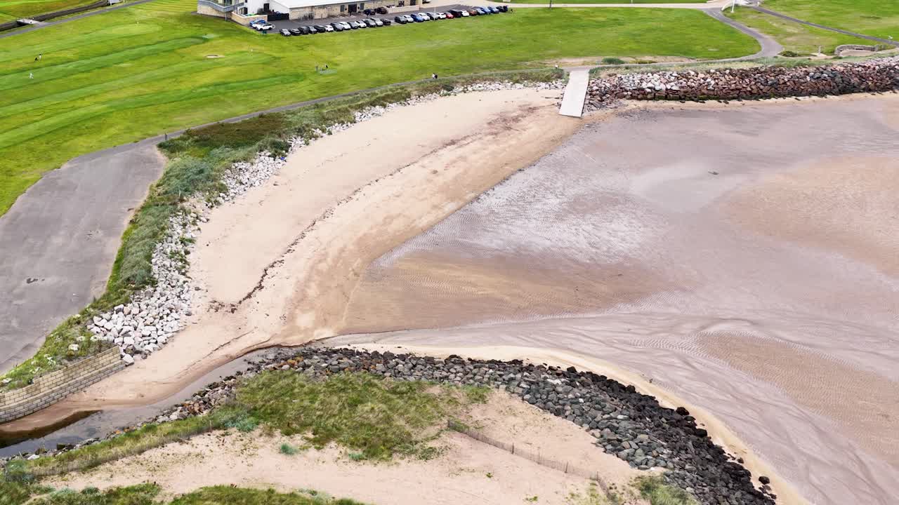 Smooth drone shot reveals golf greens, sandy beach, and clubhouse in bright daylight