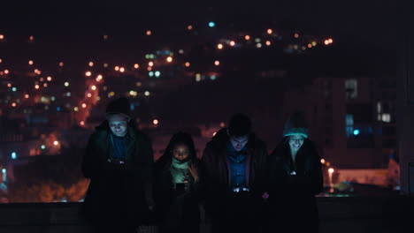 group of friends relaxing on rooftop at night using smartphone technology browsing social media chatting online enjoying weekend gathering