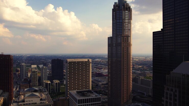 Veduta aerea con drone di un'alta torre nel centro di Chicago, circondata da una fitta architettura cittadina, nuvole drammatiche e la calda luce dell'ora d'oro.