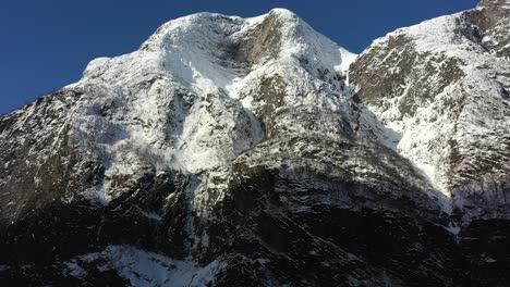 inclinación aérea hacia arriba para revelar la majestuosa montaña cubierta de nieve fetanipa sobre el fiordo naeroyfjord de la unesco en gudvangen noruega