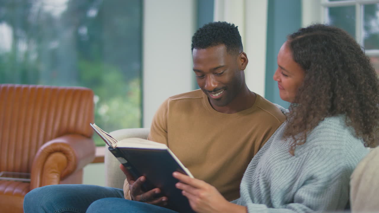 Young Couple Relaxing On Sofa At Home Looking Through Photo Album Together