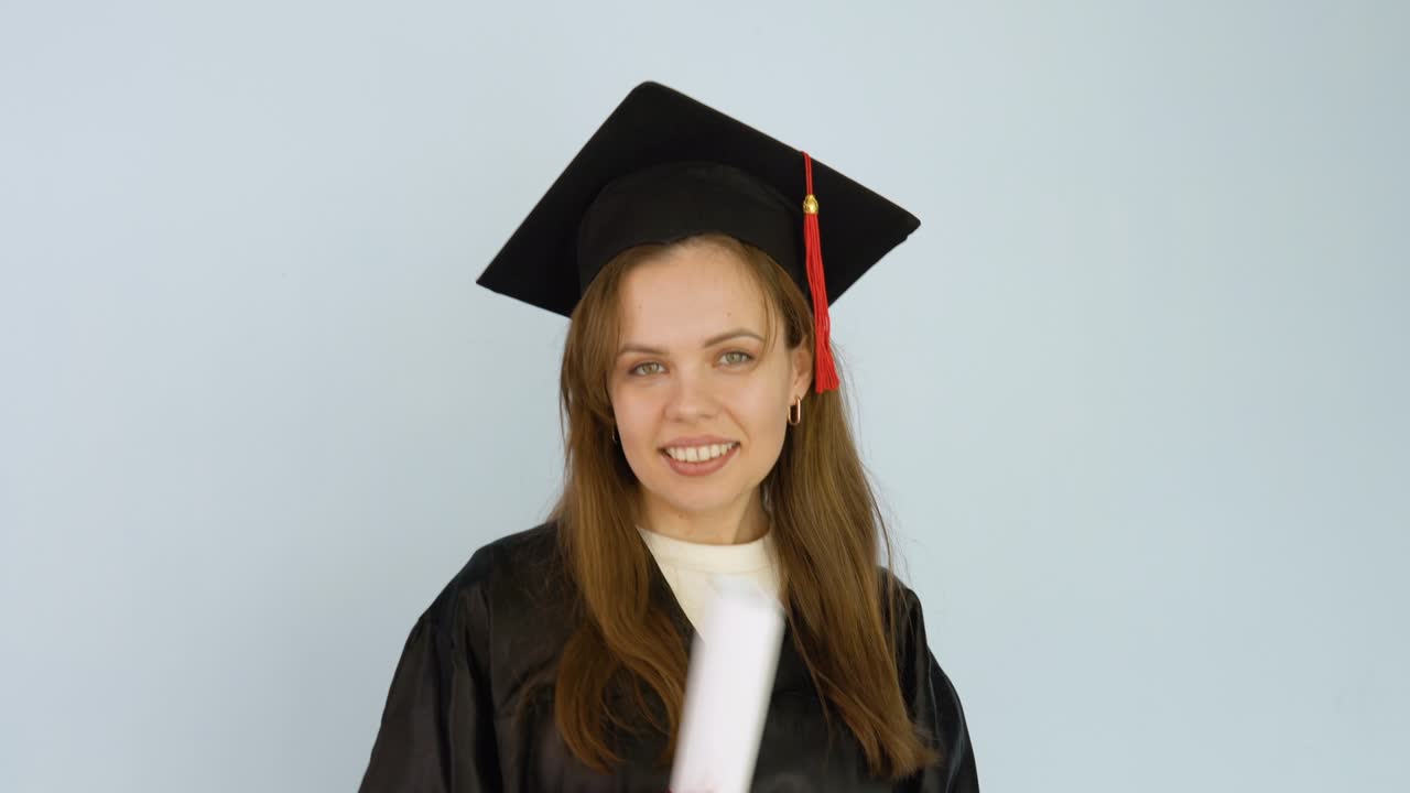 молодая студентка в черном платье и шляпе магистра с дипломом о высшем образовании. выпускник университета танцует с дипломом в руках и бросает его вверх и ловит его. белый фон