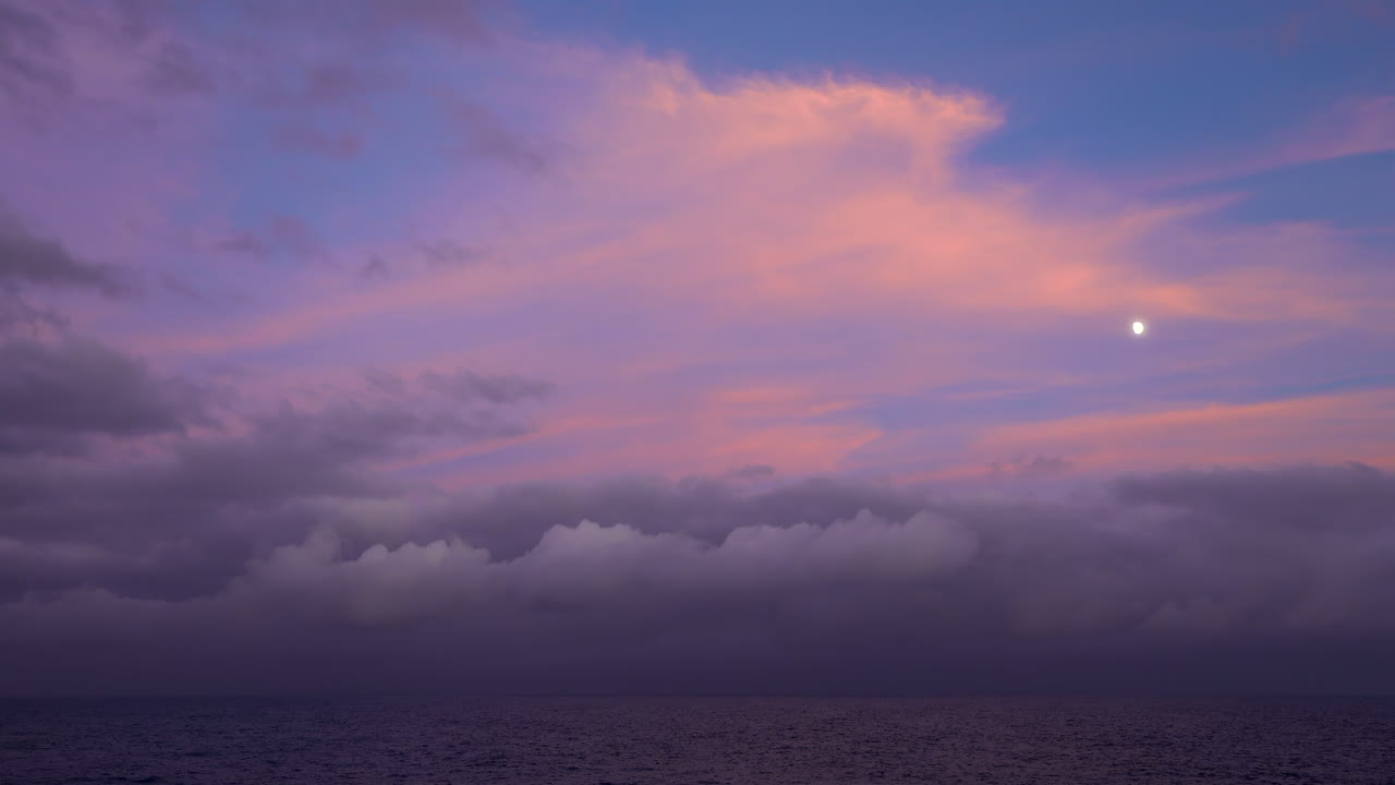 Serene view of the moon and pastel pink clouds over the Mediterranean Sea at dusk