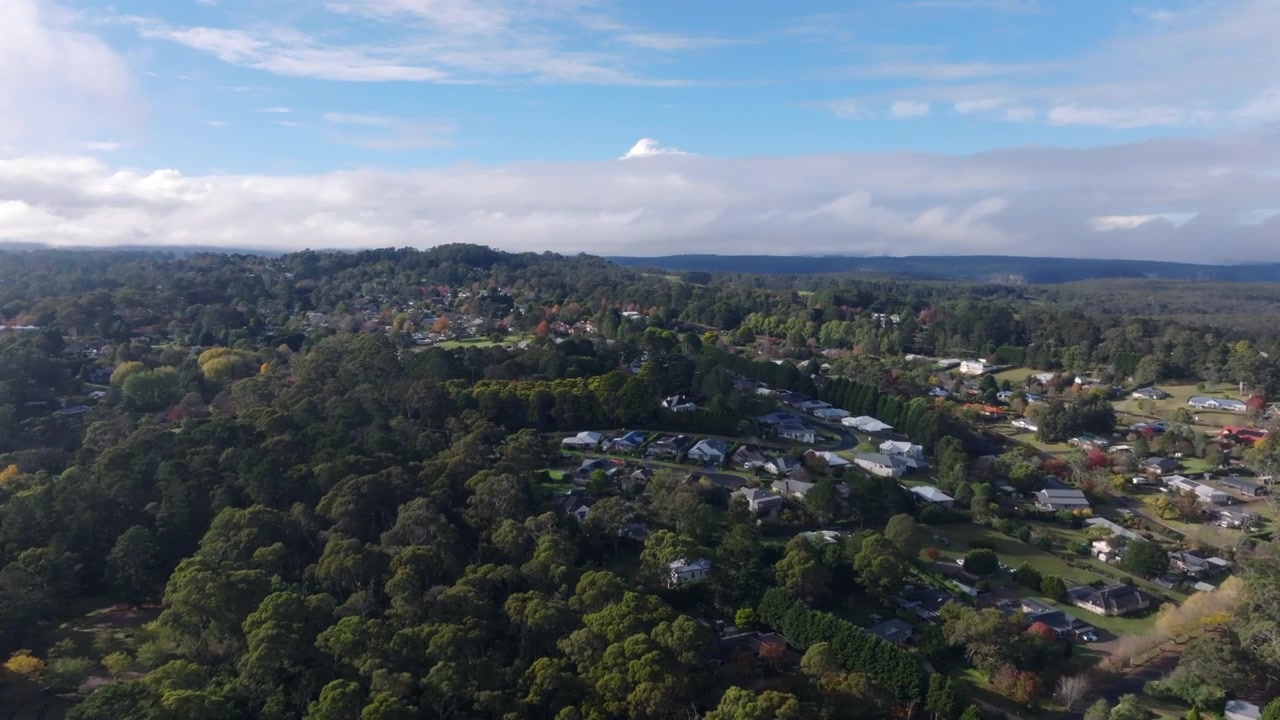 Ripresa aerea con drone che rivela lentamente la cittadina di Bundanoon circondata da foresta nativa e colline ondulate nelle Southern Highlands del Nuovo Galles del Sud, Australia