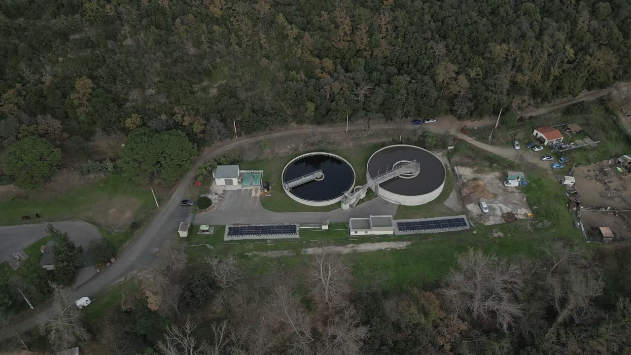 Circular wastewater clarifiers surrounded by solar panels amid forested landscape near amelie les bains palalda. Exemplifying sustainable water management infrastructure in rural french countryside
