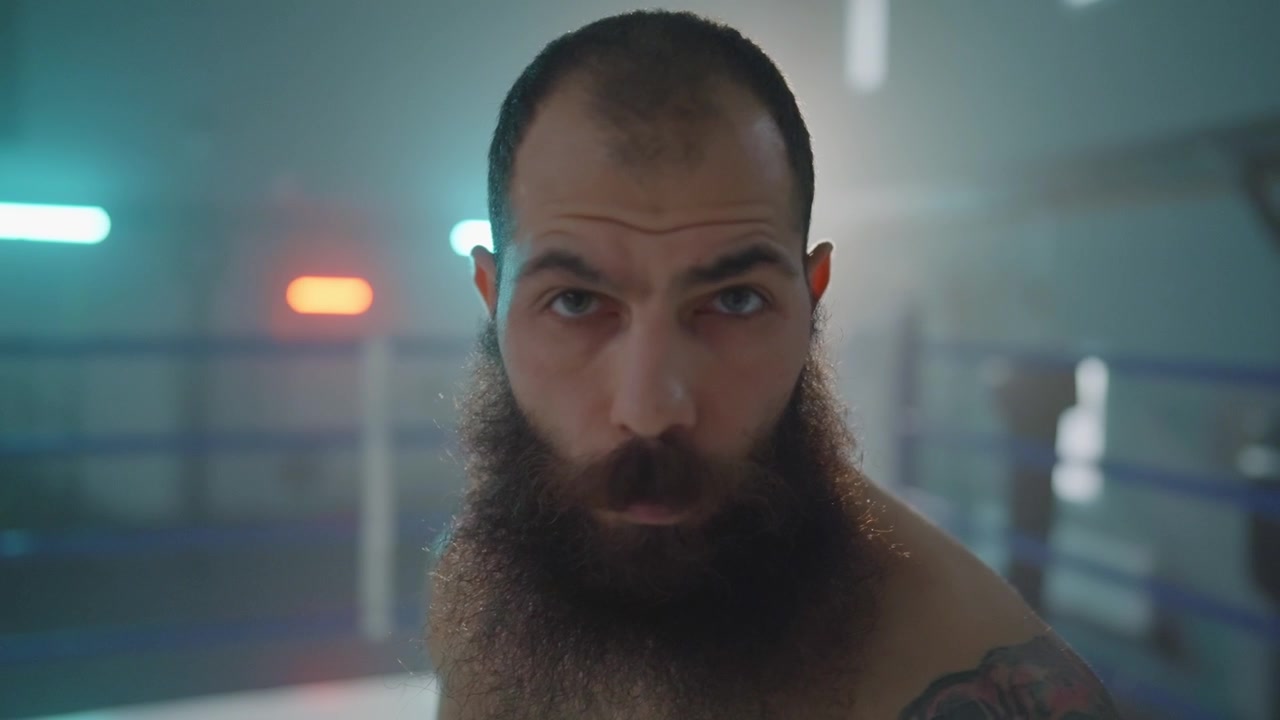Uomo barbuto dallo sguardo intenso che fissa la telecamera sul ring di boxe