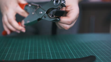 Worker-makes-holes-in-black-leather-cloth-with-punch-pliers