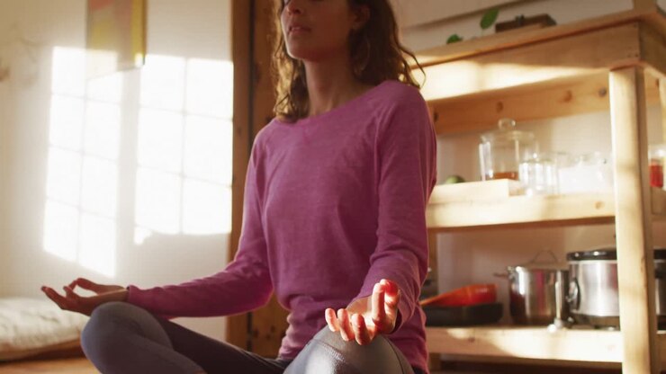 Donna di origini miste rilassata che pratica yoga, seduta in meditazione nella camera da letto soleggiata di un cottage.
