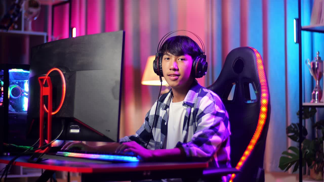 Ragazzo adolescente asiatico gamer che sorride alla telecamera mentre gioca a un videogioco al computer.