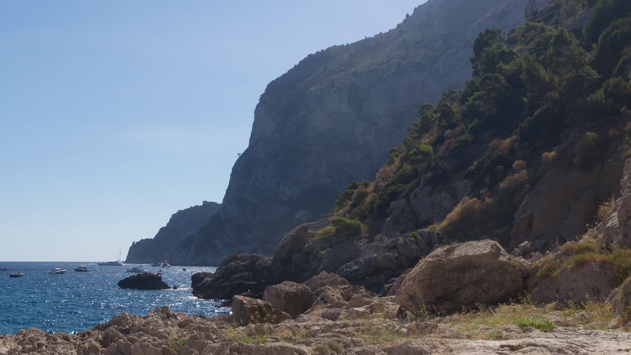 A tranquil beach scene in Capri, framed by parts of two mountains and close to the iconic Faraglioni