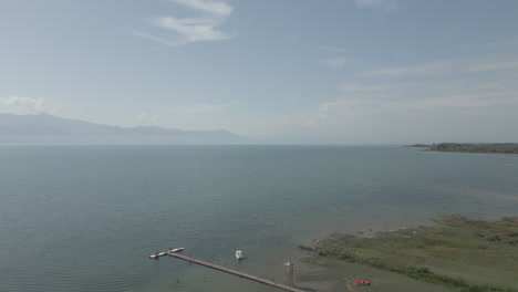 drone filmado volando sobre el lago shkodra en albania con montañas en el fondo y plantas verdes hierba naturaleza por debajo en un día soleado con niebla por encima del tronco del lago