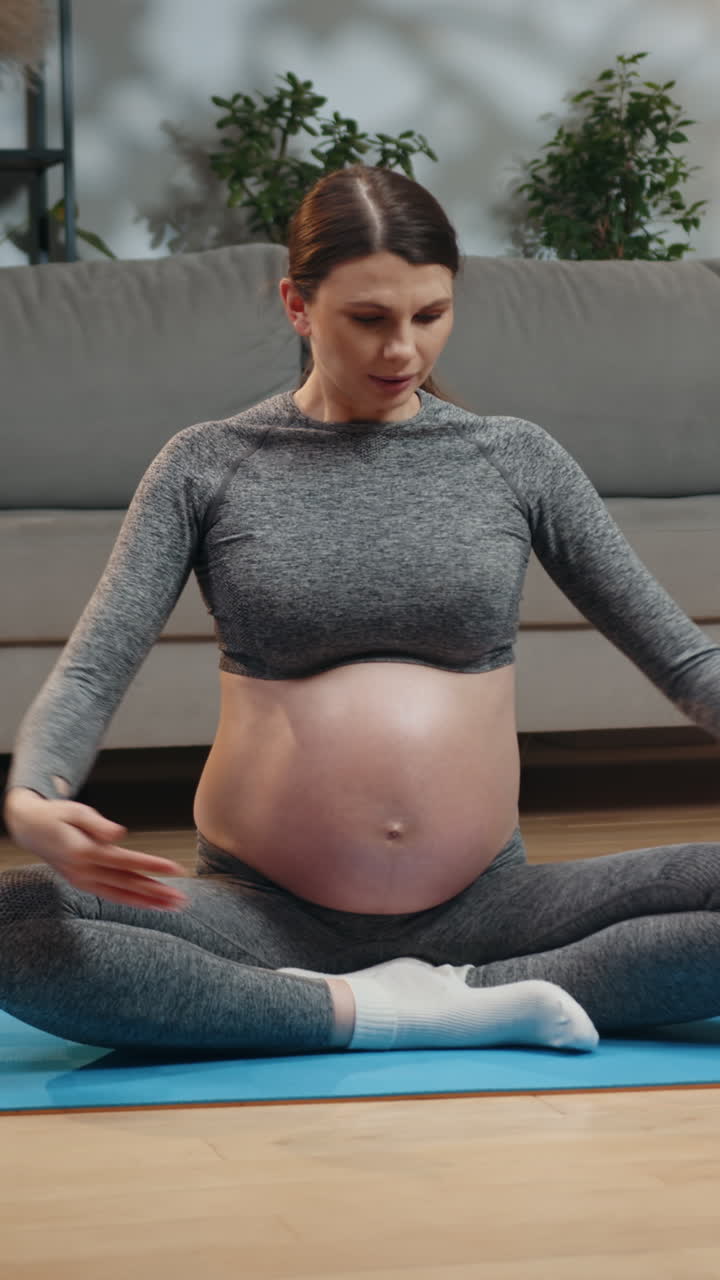 Pregnant woman sits crosslegged on yoga mat hands cradling belly practicing mindfulness and