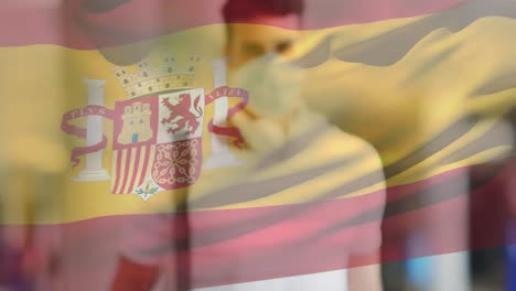 animation of flag of spain waving over man wearing face mask during covid 19 pandemic