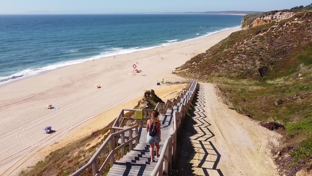 playa praia das bicas en castelo, alentejo, costa oeste de portugal - vista aérea de drones de una chica turista caminando las escaleras hacia la playa de arena dorada