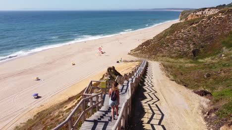 praia das bicas beach at castelo, alentejo, west coast portugal - aerial drone view of a tourist girl walking the stairs to the golden sandy beach