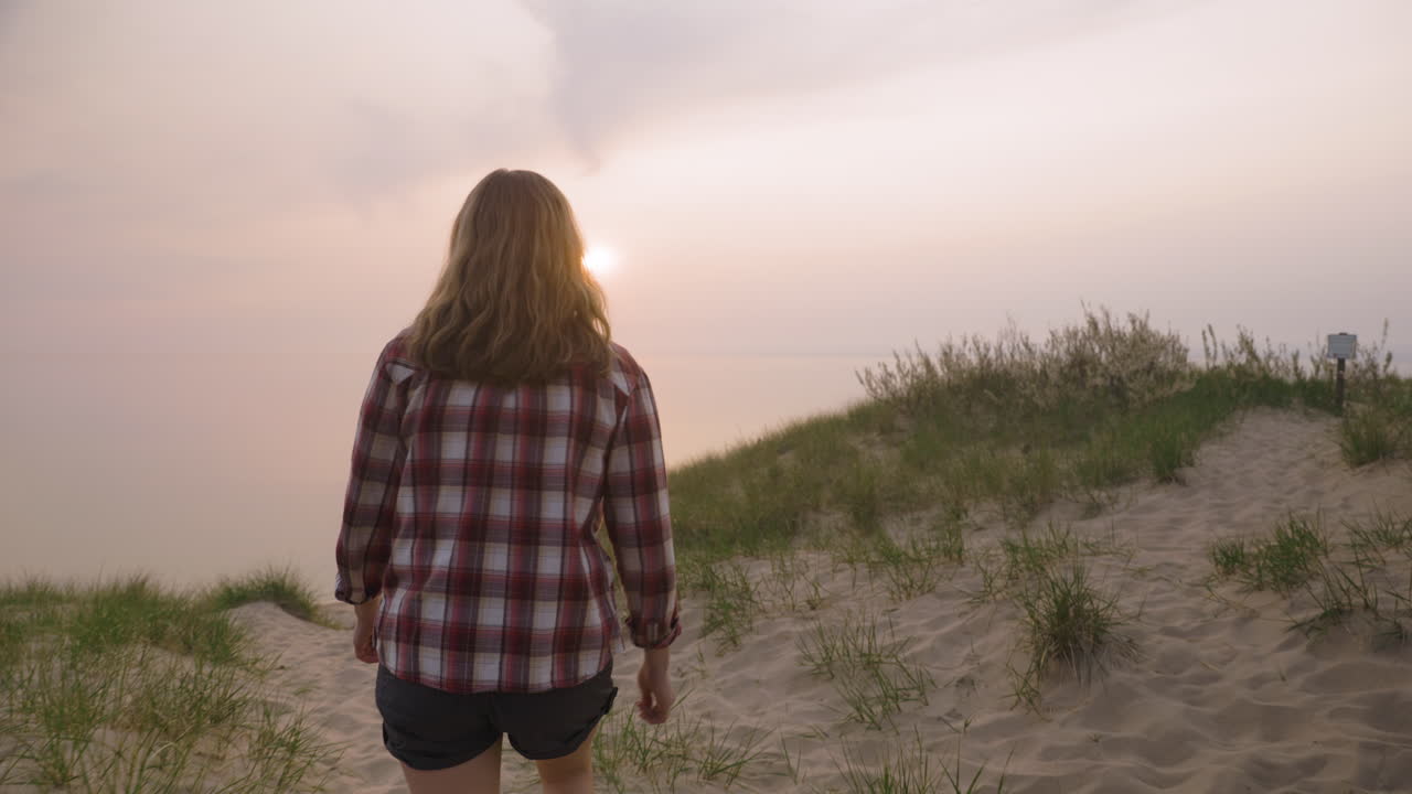 fotografía de mano de una mujer joven viendo la puesta de sol sobre un gran cuerpo de agua