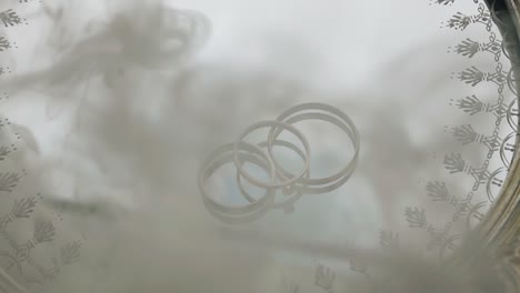smoke appears above the rings lying on a mirrored tray. he closes the rings with himself