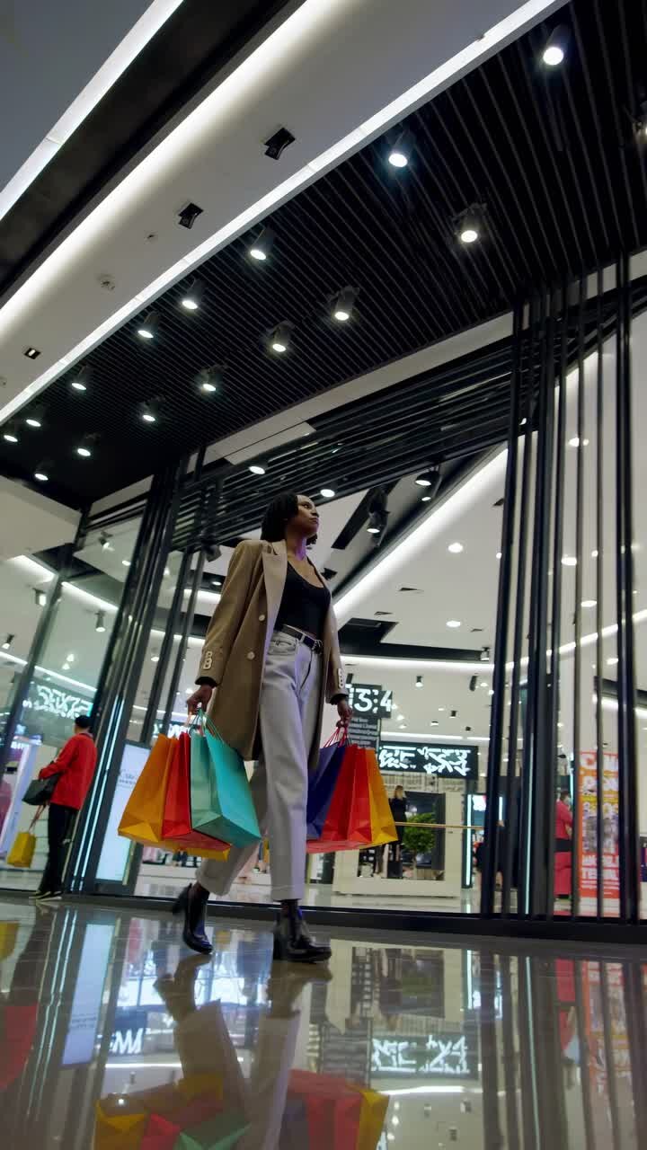 Low-angle shot of a stylish person with shopping bags in a modern mall, reflecting consumerism