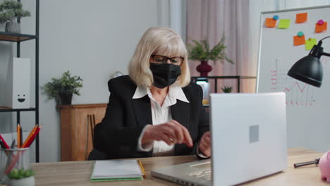 senior employee wears face mask works alone from home office sits at desk using laptop computer