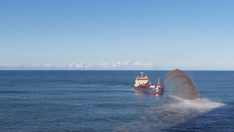 a dredger sprays sand into the ocean under clear skies, captured in a smooth aerial pan