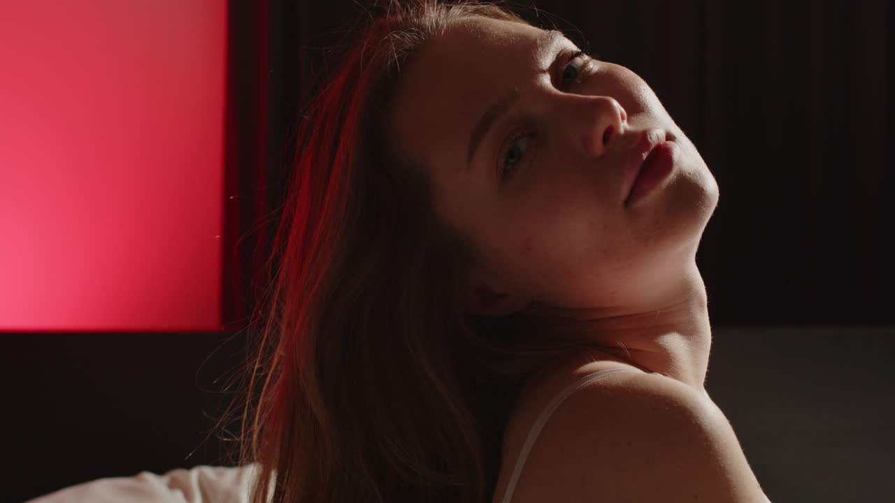 Stunning close up of a beautiful young woman sensually gazing a the the camera in slow motion while posing in bed