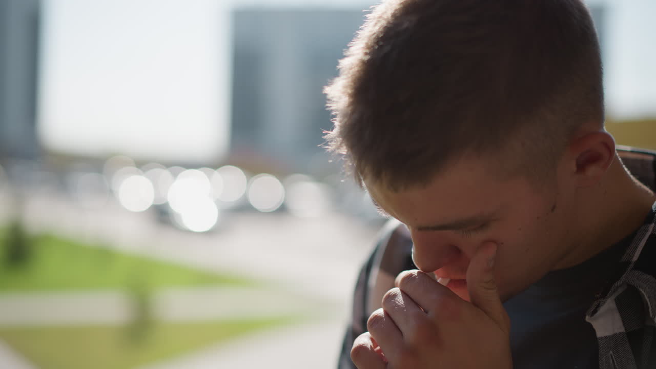 close up of young smoker with cigarette in mouth attempting to light it using hand shelter motion against soft blur background filled with bright outdoor bokeh circles and glowing daylight