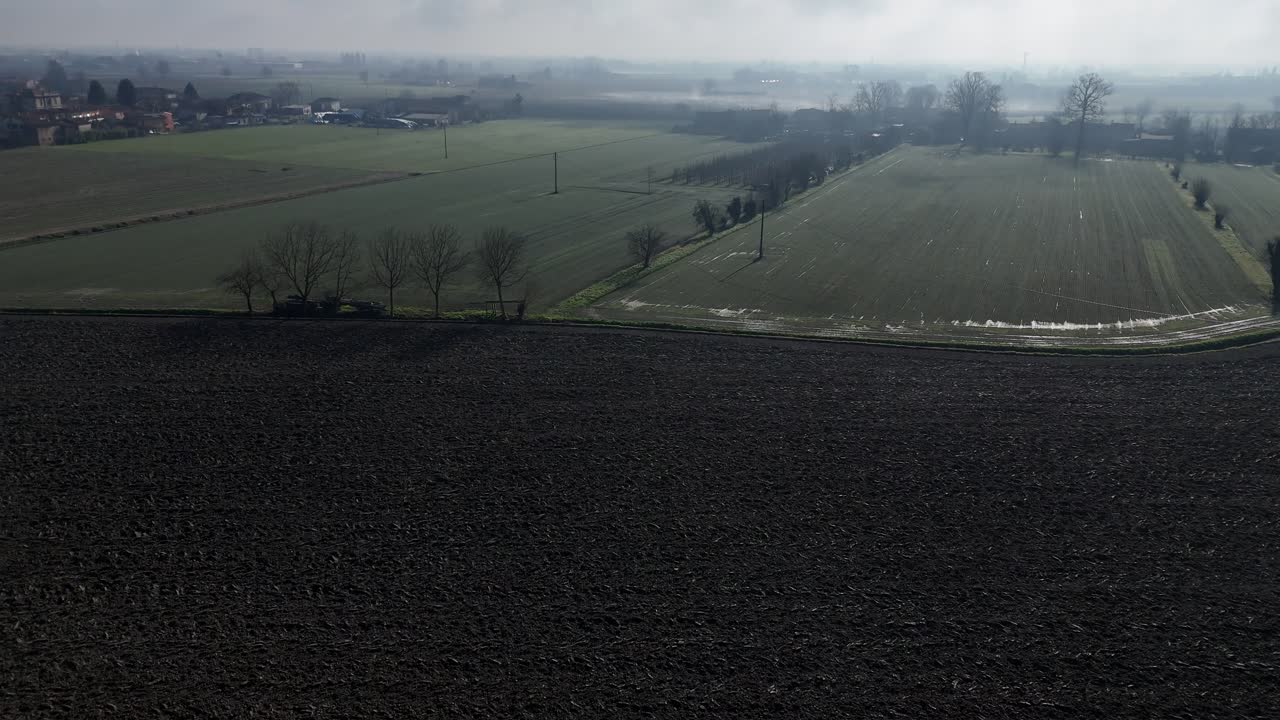 Drone shot tilting upward from textured, plowed soil to open rural farmland in the Po Valley, Piacenza province, northern Italy, showing early agricultural preparation under clear daylight, wintertime