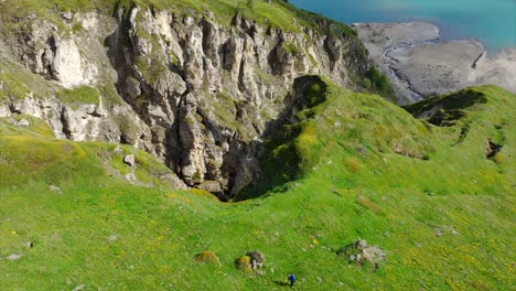 Eine-Atemberaubende-Luftaufnahme-Des-Sees-Mount-Cenis-In-Frankreich-Mit-Einem-Einsamen-Wanderer,-Der-Grüne-Hügel-Und-Schroffe-Klippen-Durchquert