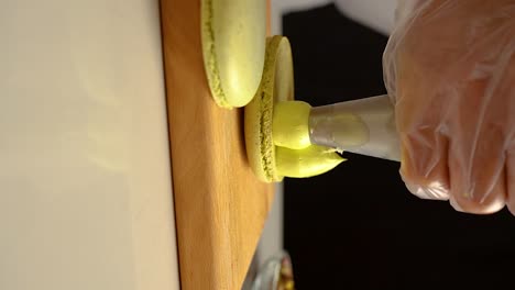 the french pastry chef adds pistachio and cream filling to the macarons , slow motion video, vertical video