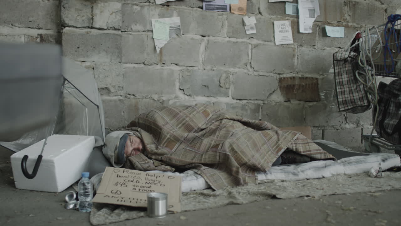 A homeless person sleeps on the street with a sign asking for help