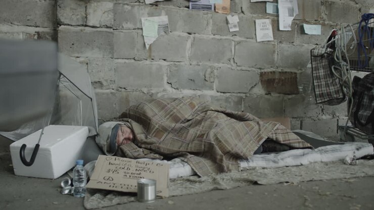 Una persona senzatetto dorme per strada con un cartello che chiede aiuto