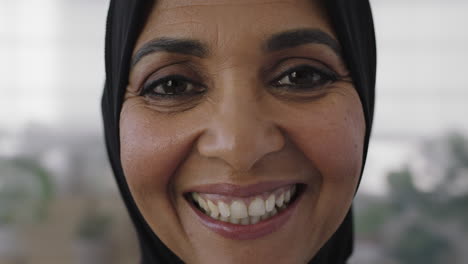 close up portrait of middle aged muslim business woman smiling looking cheerful at camera wearing traditional headscarf mature experienced female in office workspace
