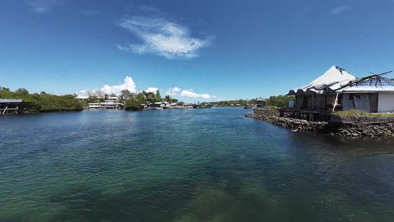 晴れた空の下、水上集落の家々の近くで、穏やかなターコイズブルーの水中をカヌーを漕ぐ男性
