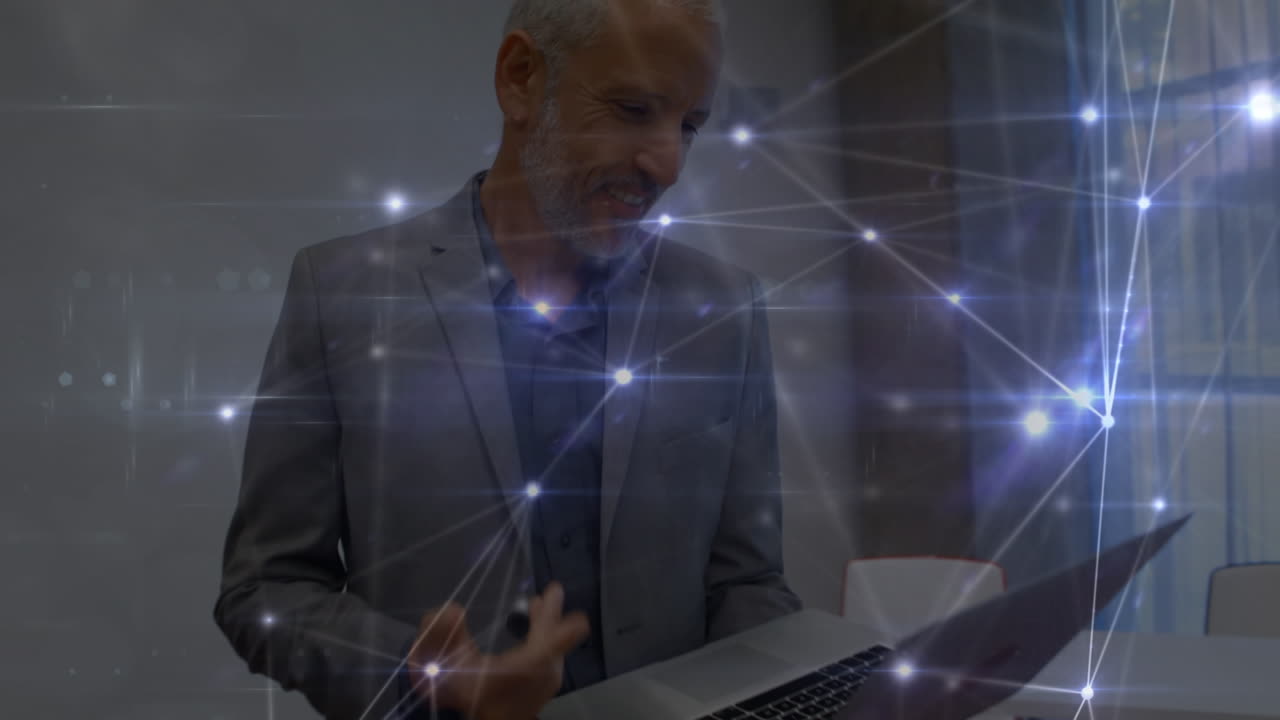 Verbindungsnetzwerk über einem kaukasischen Senior-Geschäftsmann, der im Büro einen Videoanruf über seinen Laptop tätigt.