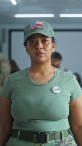 Portrait-of-female-soldier,-United-States-of-America-elections-voter.-Woman-in-camouflage-uniform-stands-in-polling-station-and-looks-at-camera.-Background-with-voting-booths.-Concept-of-civic-duty.