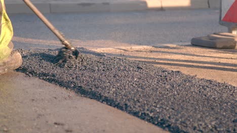 construction worker is spreading the newly poured asphalt onto the street