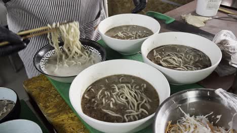 close-up of a chef using chopsticks to serve black ramen noodles into bowls in a restaurant kitchen