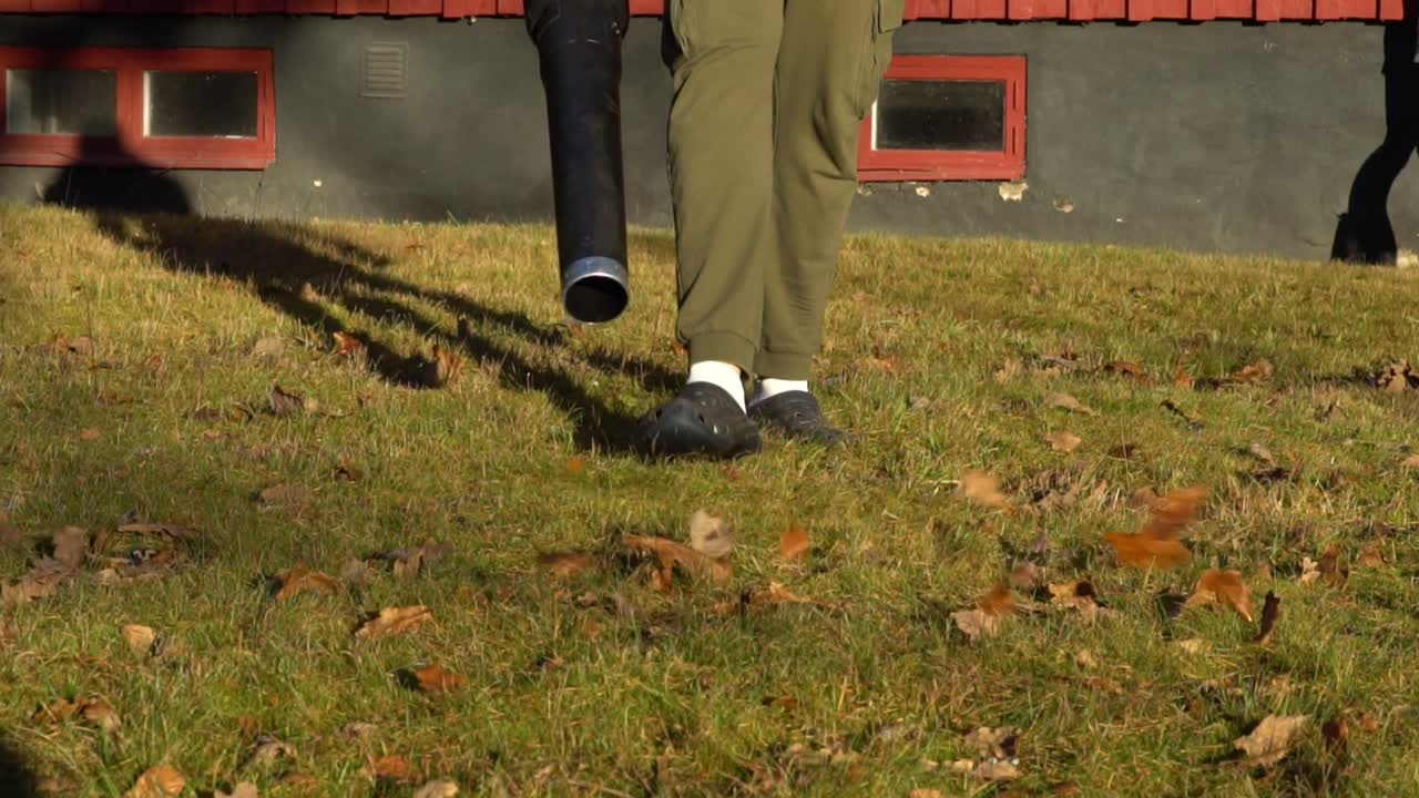 저녁에 건물 옆에 잎 송풍기가 있는 남성