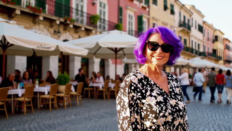 woman with purple hair smiling on a european street with an outdoor cafe