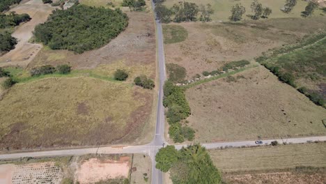 Carretera-De-La-Ciudad-Rural-Con-Cruce-De-Caminos-Cubierto-Con-Un-Coche-Solitario-Que-Pasa-Por-Una-Vista-Aérea