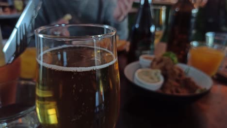 a close up shot of a glass of cider while people grab food from plates in the background