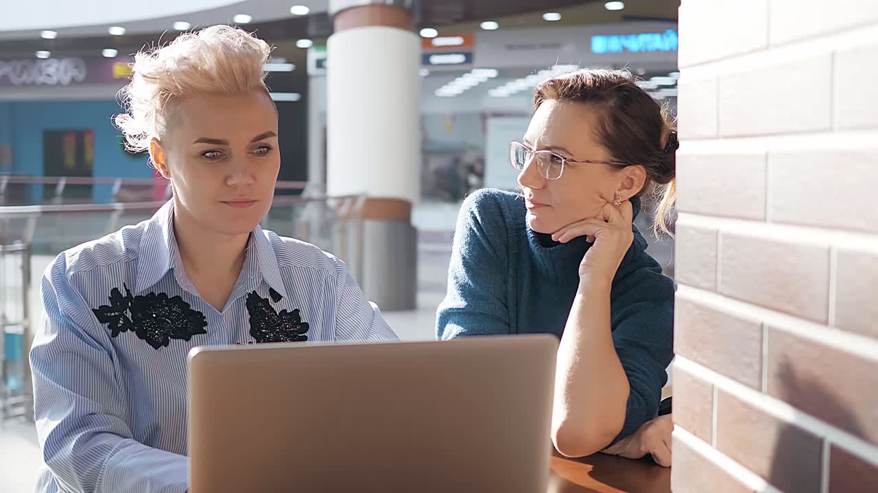 Two women working on a laptop in a mall