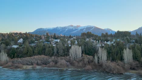 Flying-over-Lake-Nahuel-Huapi-from-the-City-of-Bariloche,-surrounded-by-its-forest-and-mountains-during-the-winter