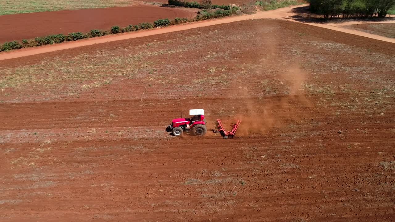 dron aéreo siguiendo desde la izquierda un tractor preparando el suelo para la siembra de semillas y mostrando todo el campo y el horizonte