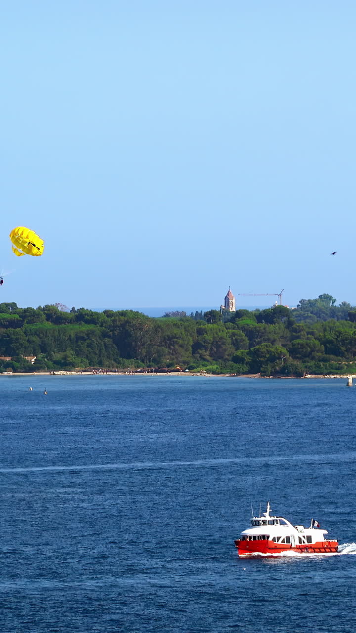 Man parasailing over boats moving on the sea in the evening in Cannes, France. Vertical