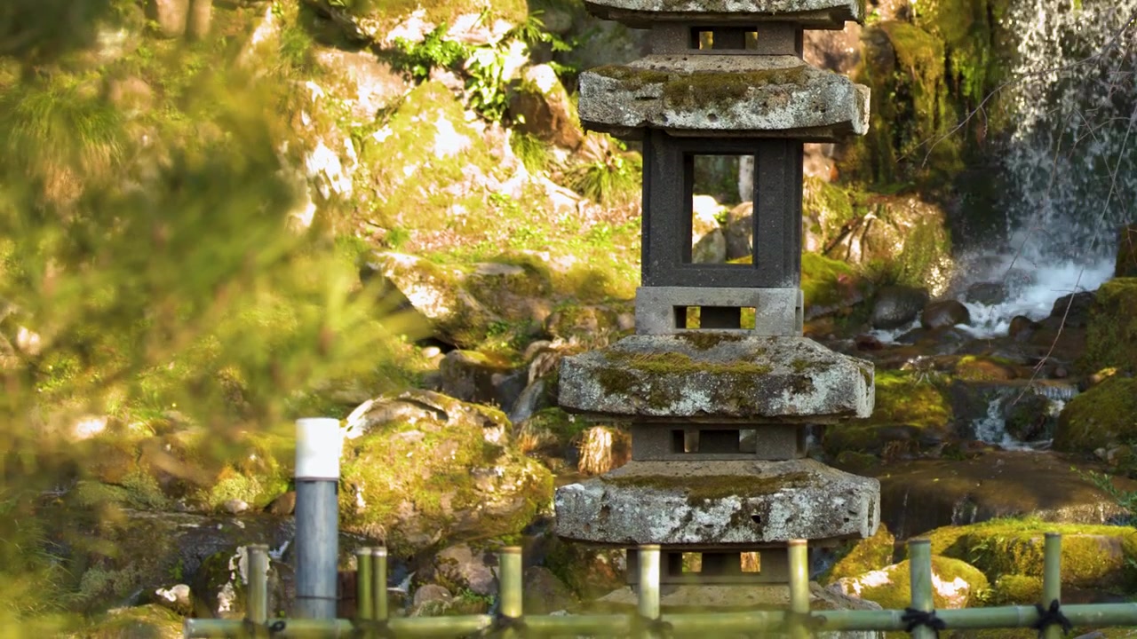 Una ripresa media statica di una lanterna di pagoda in pietra accanto a una cascata a Kanazawa