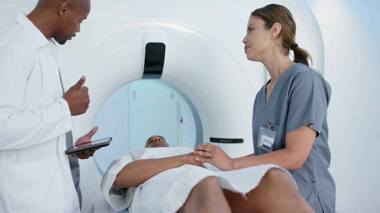 Medico in camice che consulta un tablet, tecnico in divisa medica che tiene la mano del paziente, preparandosi per la scansione.