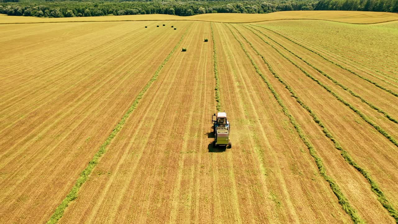 Aerial view of a tractor working on the field. Agricultural works of collecting dry grass in summer on the natural landscape.