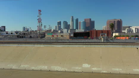 Raising-Aerial-drone-shot-from-the-LA-River-revealing-the-Downtown-Los-Angeles-Skyline-in-California-USA